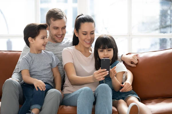 かわいい子供と幸せな親は、携帯電話を使用してソファに座ります — ストック写真
