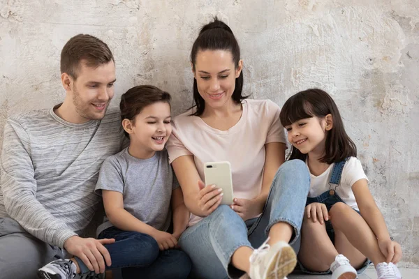 Parents heureux avec des enfants assis sur le sol en regardant le téléphone — Photo