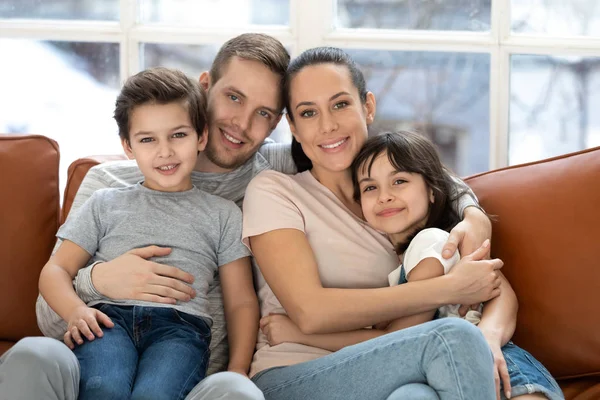 Happy föräldrar med barn bindning tittar på kamera på soffan — Stockfoto