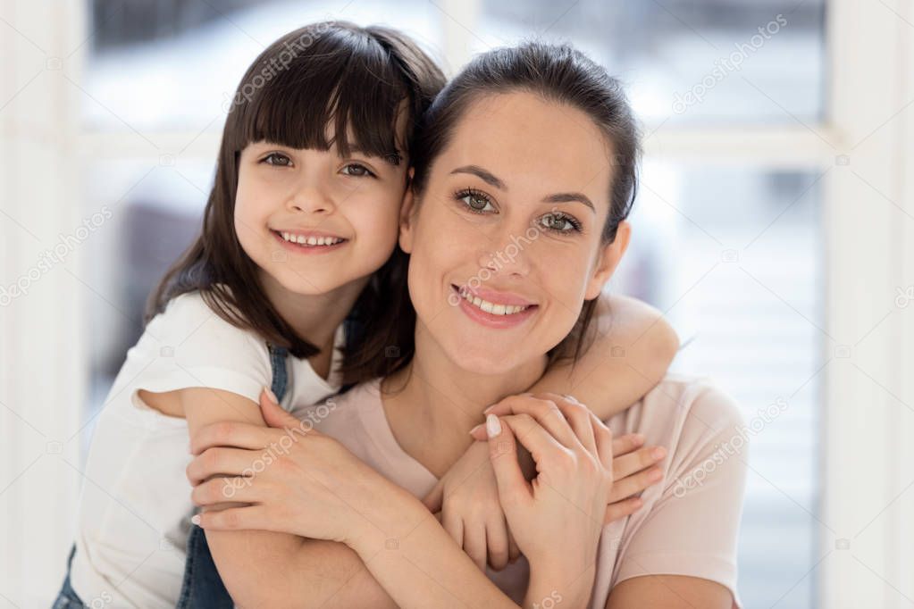 Happy kid daughter embracing mother bonding together looking at camera