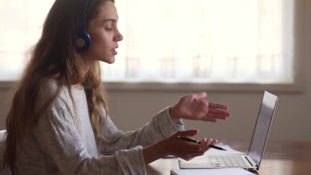 Νεαρή γυναίκα που φοράει ακουστικά μαθαίνοντας με χρήση υπολογιστών και τηλεδιασκέψεων εφαρμογές — Αρχείο Βίντεο