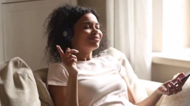Afrikalı kadın kanepede akıllı telefon kulaklıkkullanarak müzik dinleme eğildi