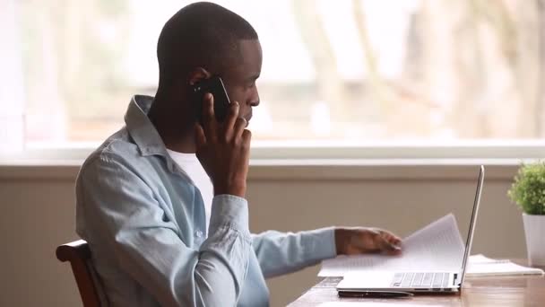 Africano freelancer uomo fare scartoffie parlando al telefono con il cliente — Video Stock