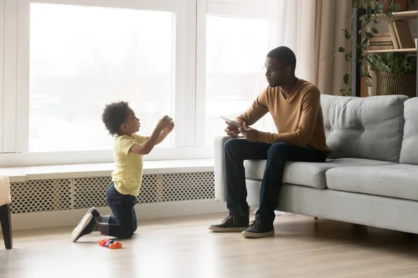 Lindo niño afroamericano hijo mostrando juguetes a padre —  Fotos de Stock