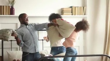 Çocuklu afrikalı aile yatakta yastık kavgası oynuyor