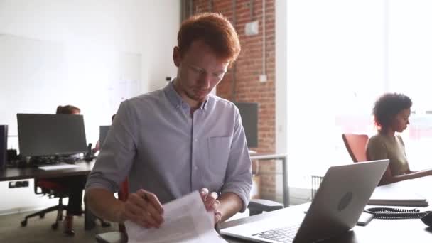 Rothaarige Angestellte prüft Dokumente, die Vereinbarungspapiere vorbereiten, die auf Laptop getippt werden — Stockvideo