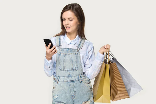 Adolescente chica mantenga bolsas de compras comprar en línea utilizando el teléfono inteligente — Foto de Stock