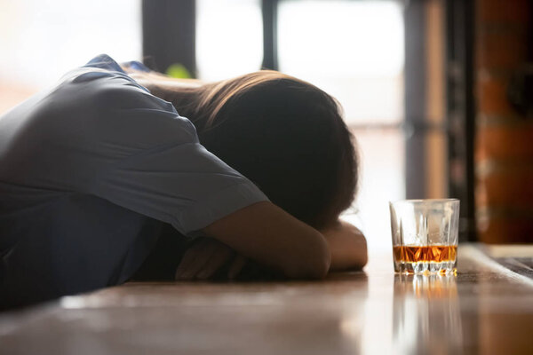 Drunk young woman sleeping on bar counter near whiskey glass
