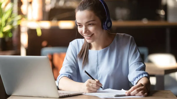 Uśmiechnięta dziewczyna nosić bezprzewodowe słuchawki badania online z nauczycielem Skype — Zdjęcie stockowe