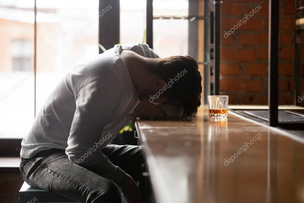 Depressed drunk young addicted man drinker sleeping alone in bar