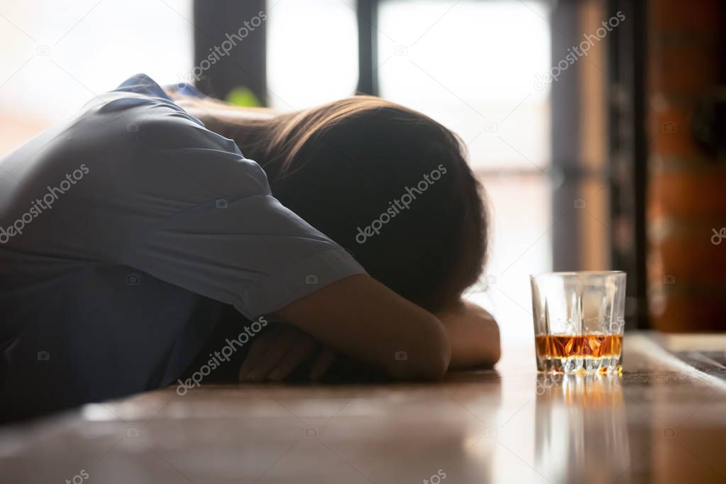 Drunk young woman sleeping on bar counter near whiskey glass