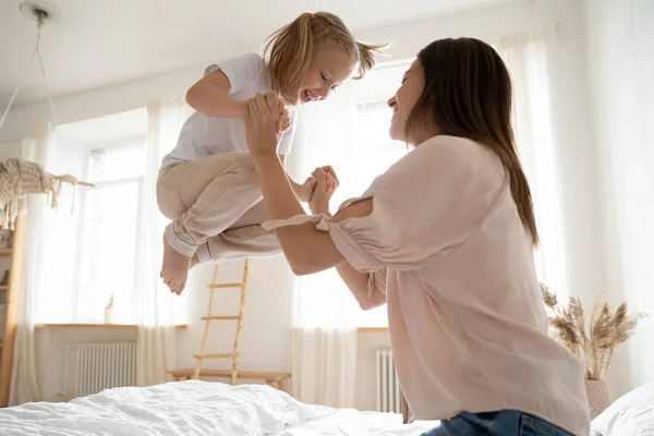 Active little girl jumping in bed holding mother hands — Stock Photo, Image