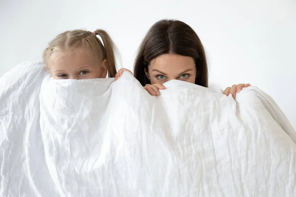 Moeder en dochter schuil achter witte deken binnenshuis — Stockfoto