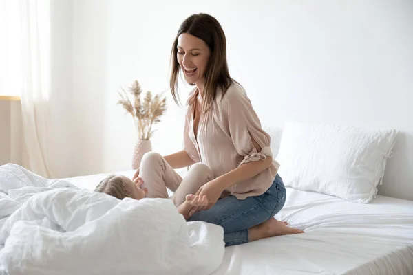 Alegre madre jugar con su hijita en la cama en casa —  Fotos de Stock