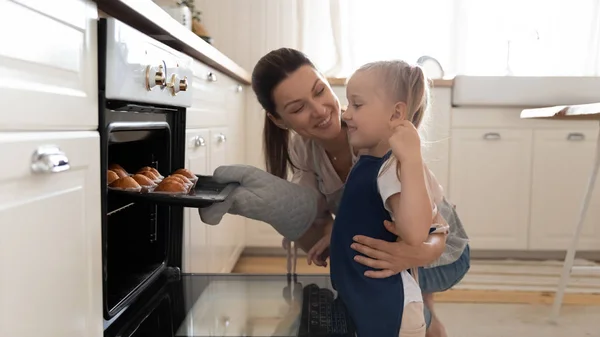 Menina e bela mãe levando muffins para fora do forno — Fotografia de Stock