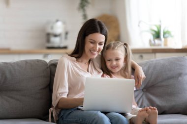 Genç anne ve okul öncesi kızı dizüstü bilgisayar ile kanepede oturan