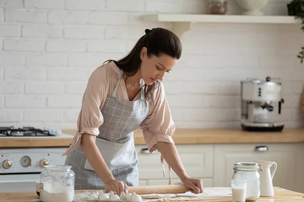 Ama de casa de pie sobre la mesa de la cocina aplanando la masa con rodillo — Foto de Stock