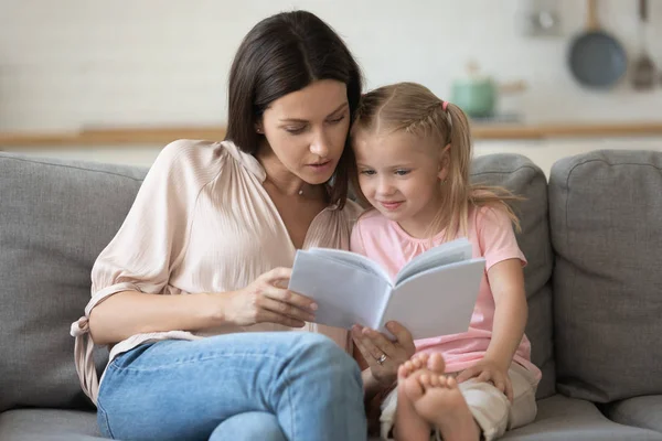 Madre e hija sentadas en un sofá leyendo un libro — Foto de Stock