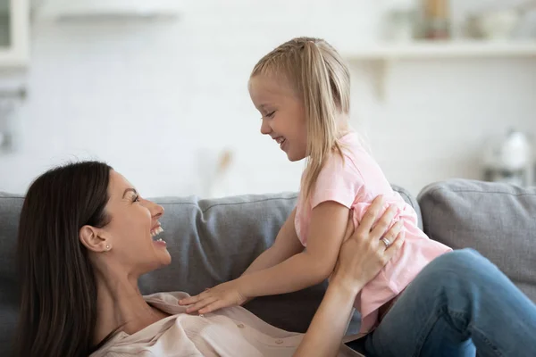 Gioviale madre giocando con la piccola figlia sdraiata sul divano — Foto Stock