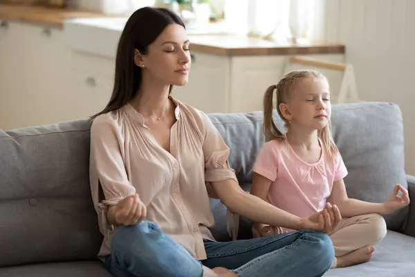Ibu dan anak dalam posisi teratai melakukan meditasi di sofa — Stok Foto
