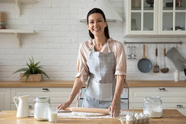 Woman holding rolling pin flattening dough looking at camera — Stock Photo, Image