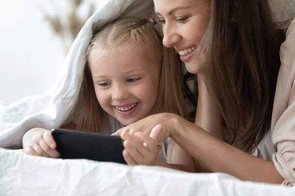 Anne ve kızı akıllı telefon ile battaniye altında yatakta yatarken — Stok fotoğraf