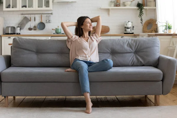 У затишній вітальні щаслива жінка сидить на дивані сама — стокове фото