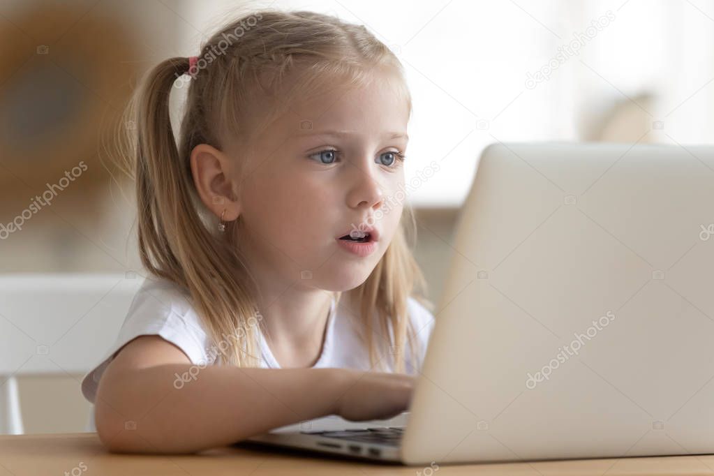 Little girl sitting at table watching cartoons on laptop