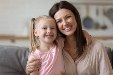 Güzel anne sarılmak kızı aile kamera bakarak kapalı oturan