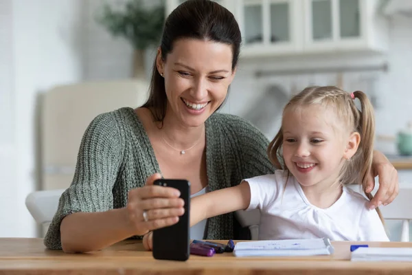 Mulher e filha se sentam à mesa na cozinha com smartphone — Fotografia de Stock