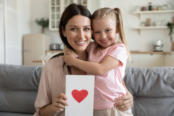 Щаслива мати тримає листівку з червоним серцем обіймає дочку — стокове фото