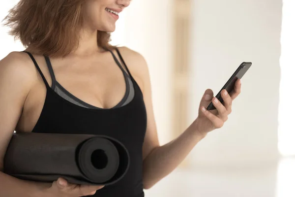 Uśmiechnięta kobieta instruktor fitness trzyma Mata do jogi, za pomocą telefonu — Zdjęcie stockowe