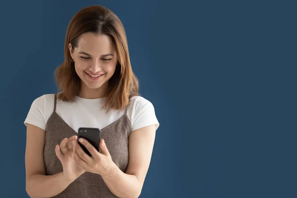 Smiling woman looking at phone screen isolated with blue copy space