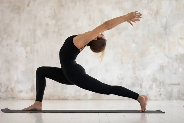 Młoda kobieta uprawia jogę, stojąc w Warrior one Pose, Virabhadrasana — Zdjęcie stockowe