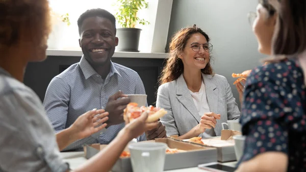 Lykkelig africaner og hvite forretningsfolk som deler pizza på kontoret – stockfoto