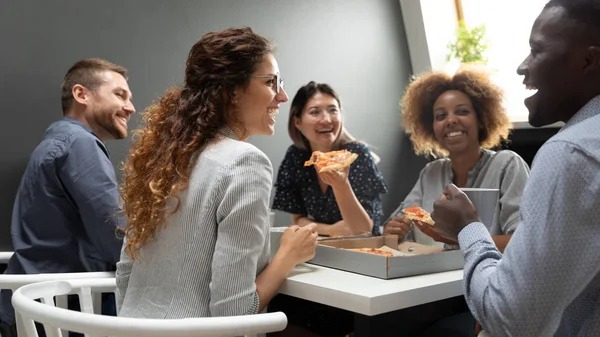 Веселая многорасовая команда бизнесменов веселится, поедая пиццу вместе — стоковое фото
