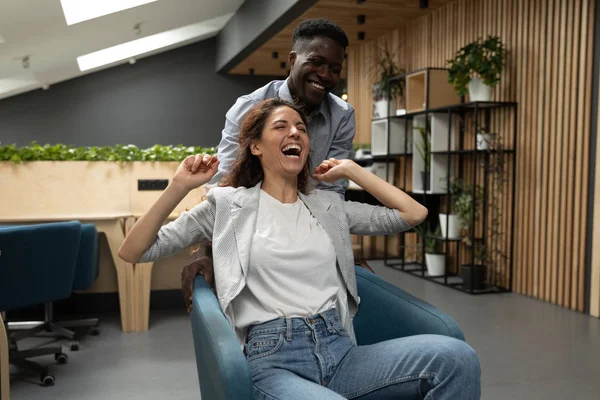 Diversos colegas felizes rindo andando na cadeira no escritório — Fotografia de Stock