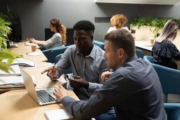 Африканські та кавказькі колеги обговорюють проект з використанням ноутбука в офісі — стокове фото
