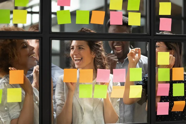 Alegre equipo de negocios diverso de pie detrás de vidrio con notas adhesivas —  Fotos de Stock