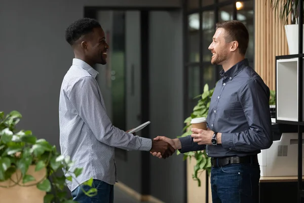 Two happy diverse male colleagues handshaking standing in modern office — Stock Photo, Image