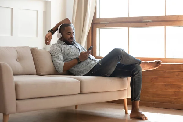 Uomo nero che si rilassa sul divano a casa, ascoltare musica . — Foto Stock