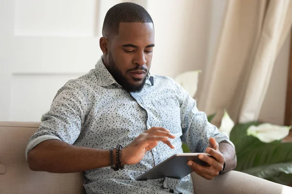 Concentrado joven afroamericano hombre sosteniendo tableta digital . — Foto de Stock