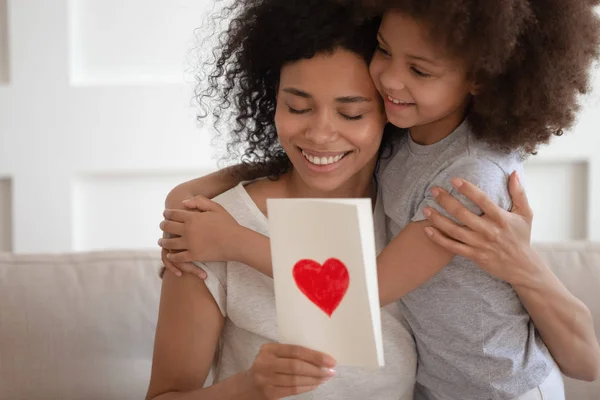 Heureuse mère afro-américaine étreignant sa fille, tenant sa carte de vœux . — Photo