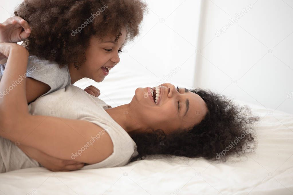 Happy black mother lying on bed, holding happy cute daughter.