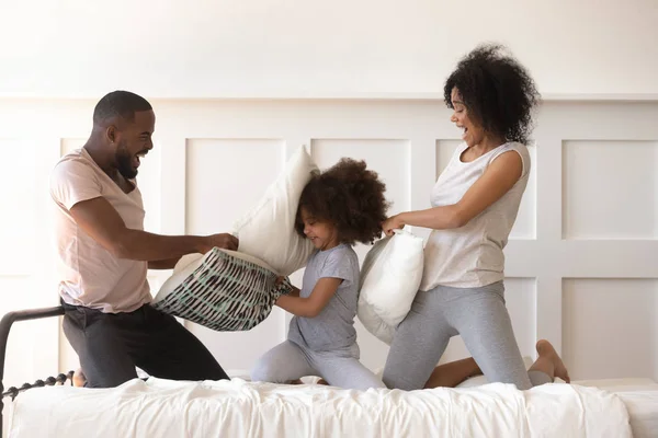 Lycklig afrikansk amerikansk familj slåss med kuddar på sängen. — Stockfoto