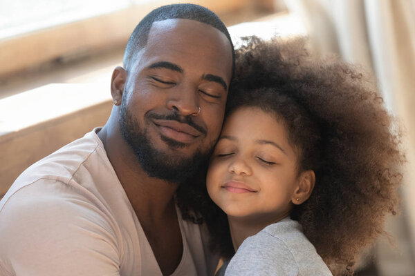 Close up head shot young black man embracing little daughter.