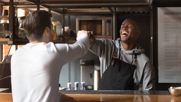 Laughing African American barista fists bumping with customer in cafe — Stock Photo, Image