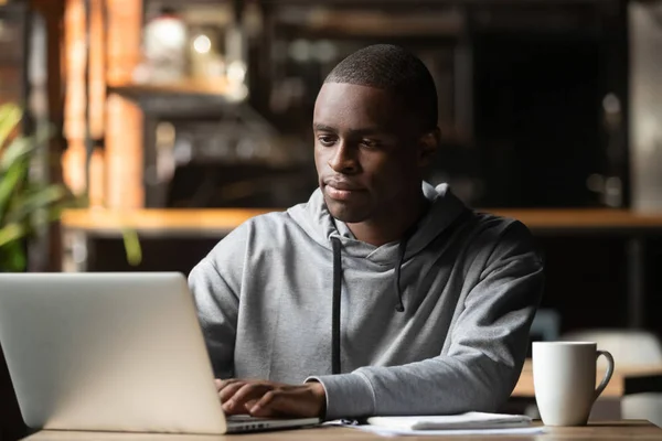 Uomo afroamericano che utilizza il computer portatile in caffè, guardando lo schermo — Foto Stock