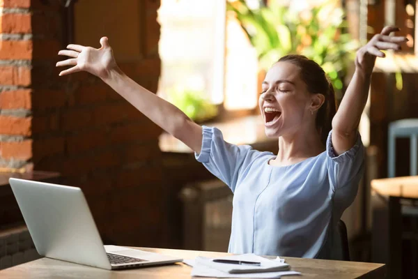 Захоплена усміхнена жінка, яка святкує онлайн-перемогу, використовуючи ноутбук у кафе — стокове фото