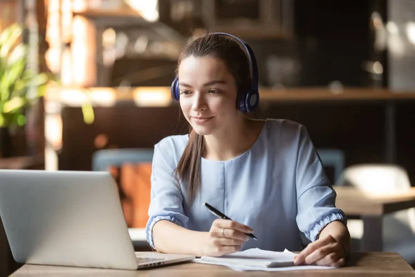 Mulher focada usando fones de ouvido usando laptop, escrevendo notas — Fotografia de Stock